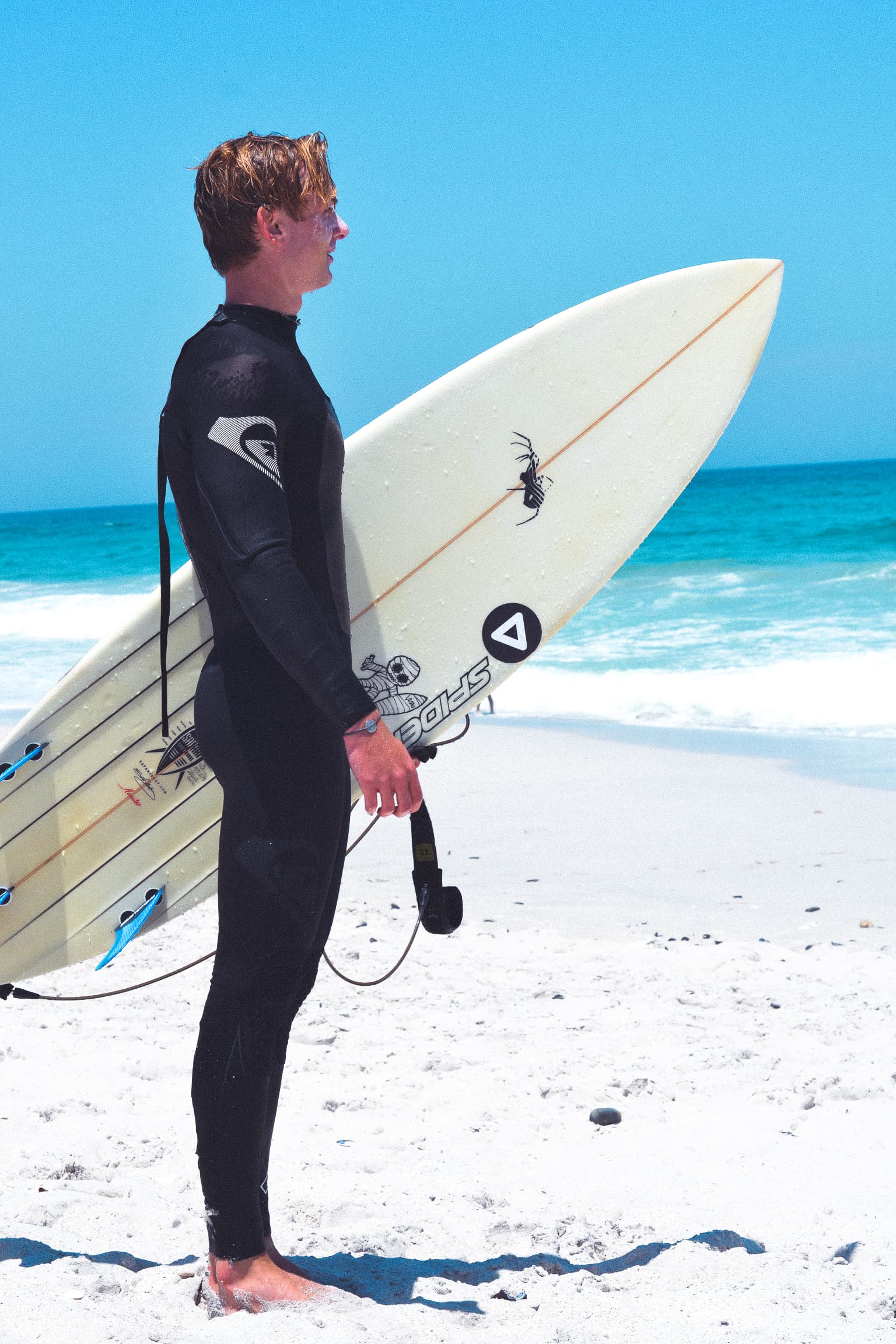 Jadon on the beach in a wetsuit, holding a surfboard.
