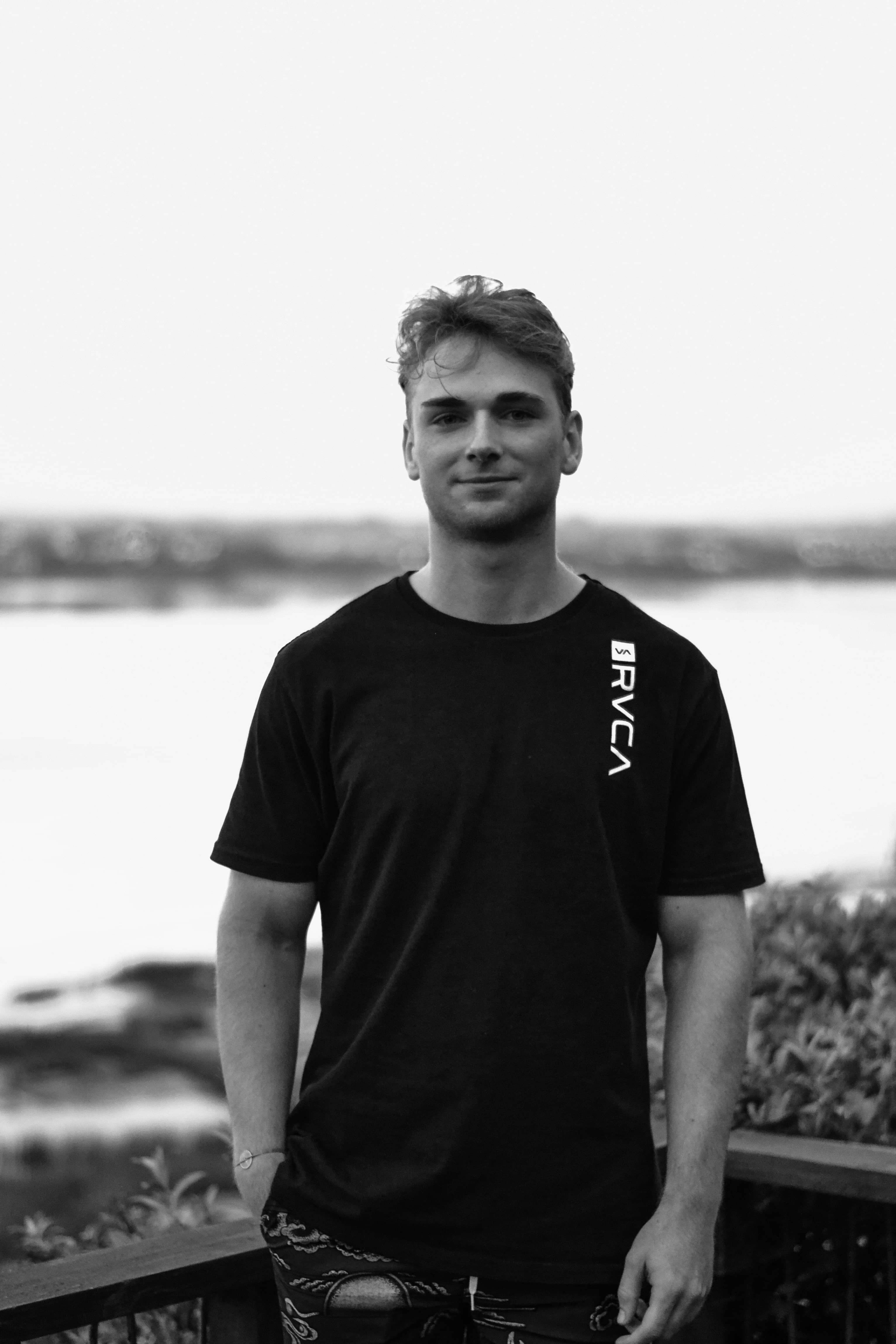 Black and white photo of Jadon in a black t-shirt, standing by the water.
